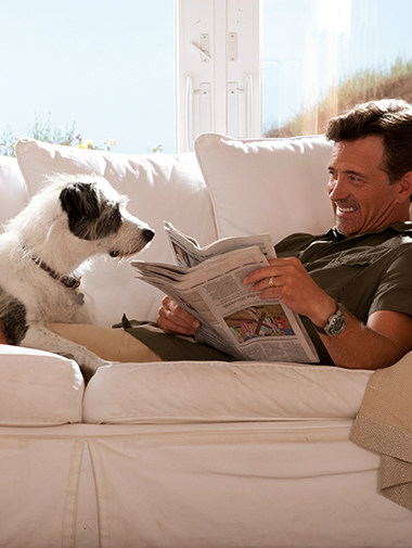 Dog laying on sofa with owner as he reads newspaper